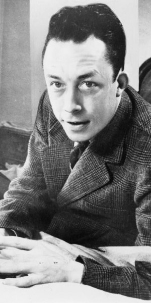 Albert_Camus,_gagnant_de_prix_Nobel,_portrait_en_buste,_posé_au_bureau,_faisant_face_à_gauche,_cigarette_de_tabagisme