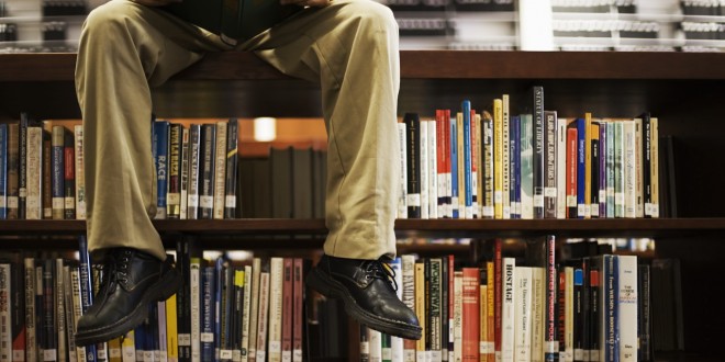 Man Reading Book and Sitting on Bookshelf in Library --- Image by © Royalty-Free/Corbis