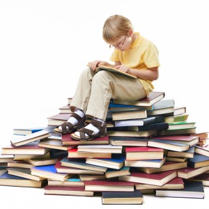 Portrait of diligent pupil sitting on top of books and reading