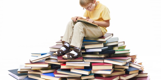 Portrait of diligent pupil sitting on top of books and reading