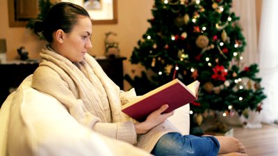 stock-footage-woman-reading-book-on-sofa-christmas-tree-in-background