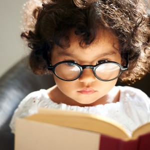 A cute little girl wearing glasses and reading a book